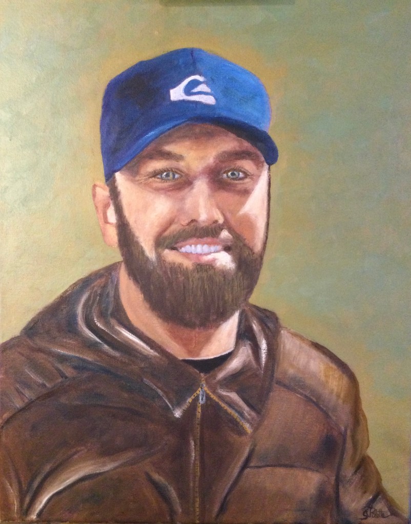 Jeune homme souriant barbu aux yeux bleus avec une casquette bleue et un manteau brun sur fond vert sauge 